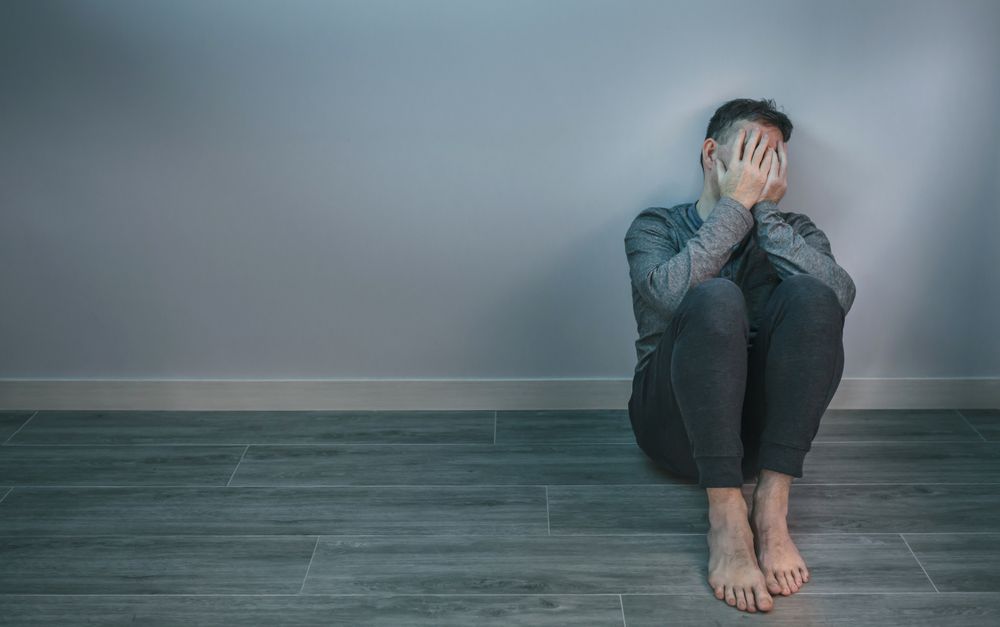Man crying while covering his face with hands sitting on the floor