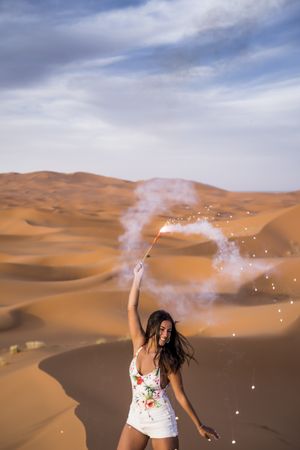 Happy woman holding firework in desert