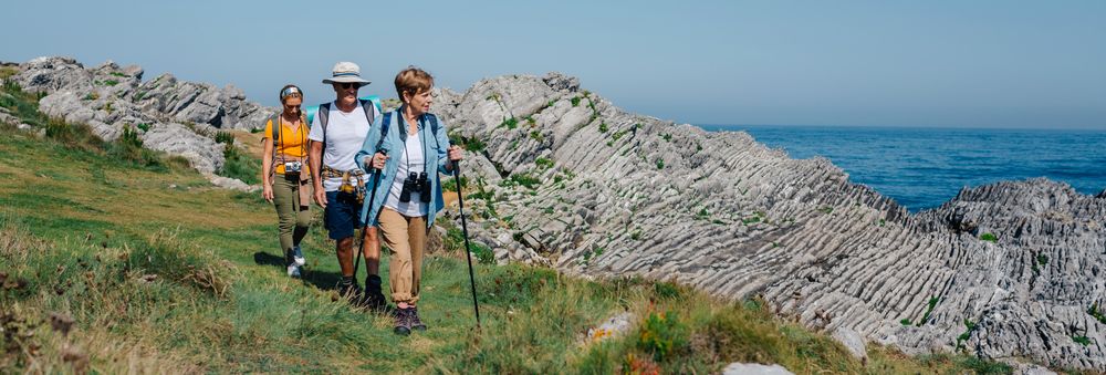Wide shot of two mature people and their daughter hiking on hill near ocean