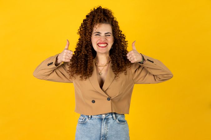 Excited woman raising two thumbs up against yellow background