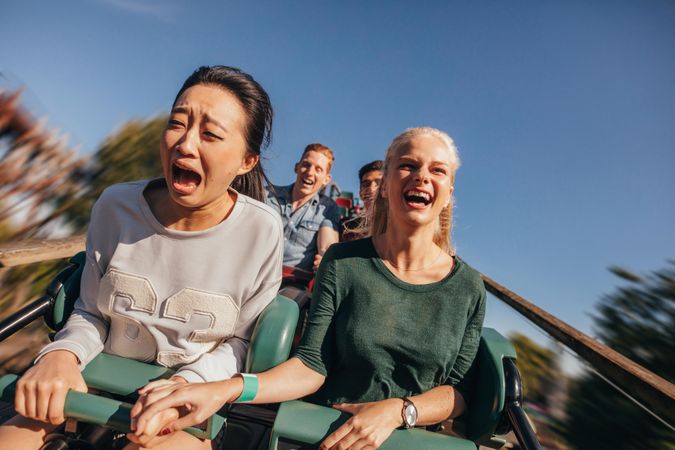 Shot of young friends cheering and riding roller coaster at amusement park