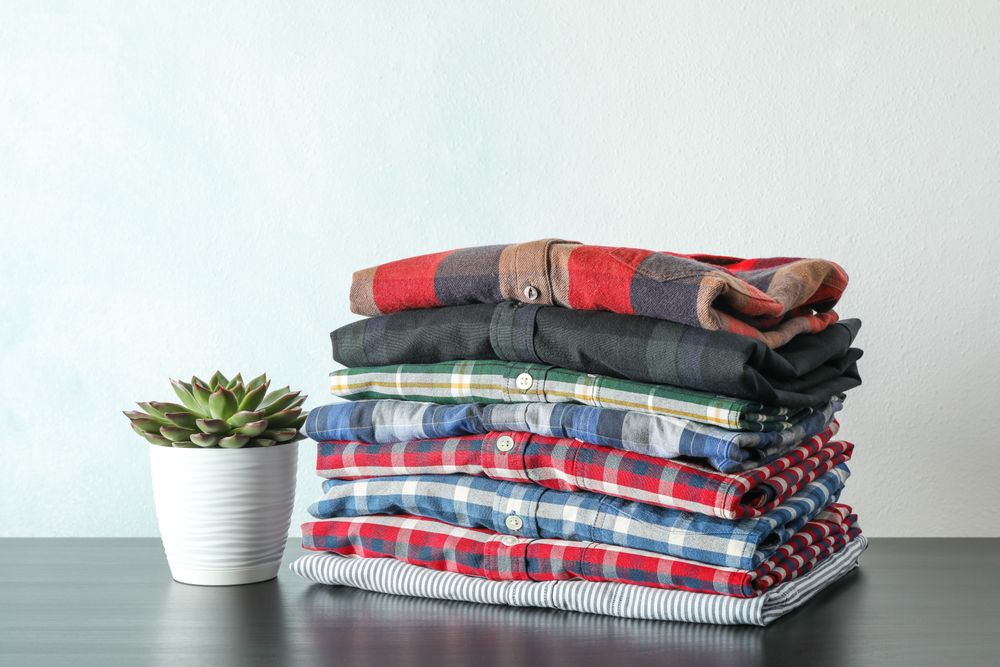 Stack of colorful shirts and succulent plant on table against light background