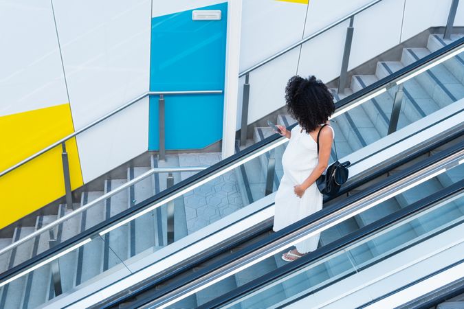 Pregnant Black woman browsing smartphone on escalator