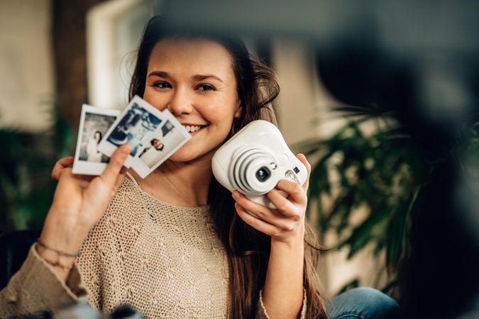 Smiling woman showing an instant camera and photographs taken on it while video recording herself
