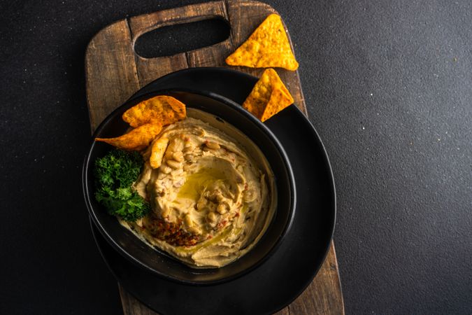 Looking down at creamy hummus dip in bowl with swirl of olive oil and chips with copy space