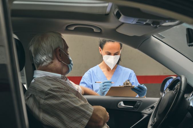Crop doctor with clipboard against mature patient in car