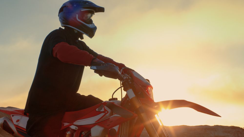 Professional FMX Motorcycle Rider Prepares to Start Driving on His Bike Over Hard Sandy Off-Road Terrain.