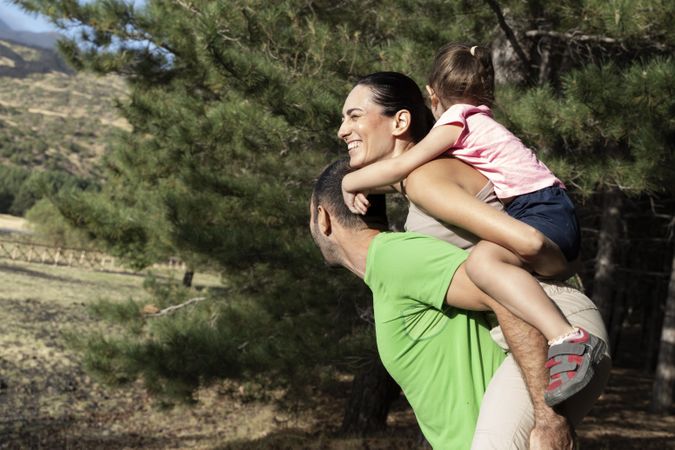 Family playing outdoors with child on mom’s back and dad supporting togetherness