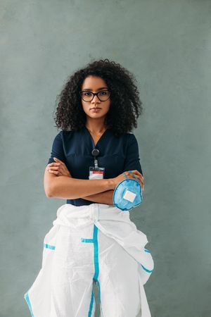 Black medical professional holding facemask with hazmat suit on the bottom half of her bottom