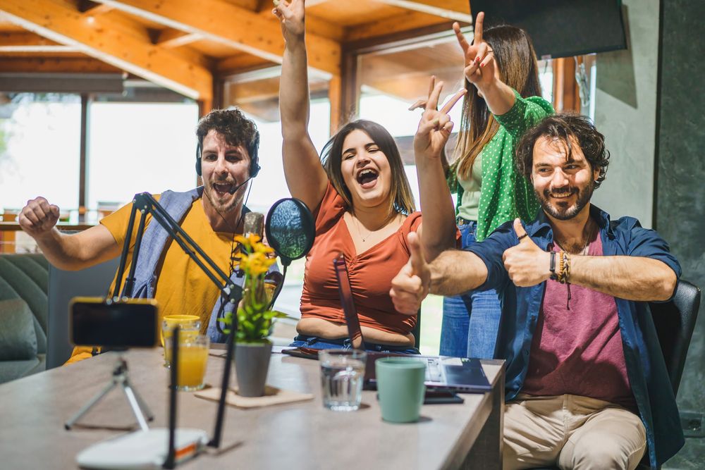 A group of four content creators jubilantly celebrate and gesture towards a smartphone mounted on a tripod