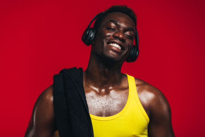 Fit young man listening to music during workout break on red background