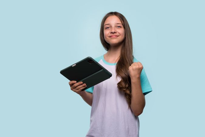Girl holding tablet, making fist to celebrate success.
