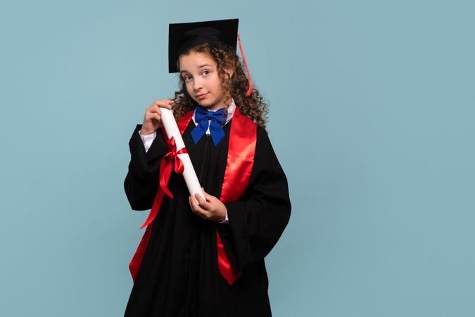Young girl in graduation gown holding diploma near her head.