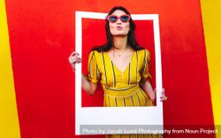 Young woman posing with photo frame against red and yellow colored wall 4ZVN34