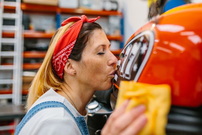 Female mechanic kissing fuel tank of motorcycle while cleaning it on factory