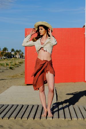 A long hair fashion model with a hat at the beach in front of a red wall