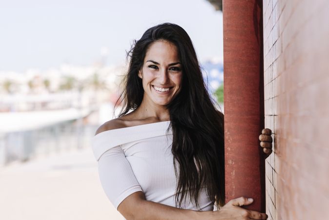 smiling young woman hanging on a pole in the street while looking camera
