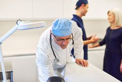 Male doctor in surgery gear preparing examination table