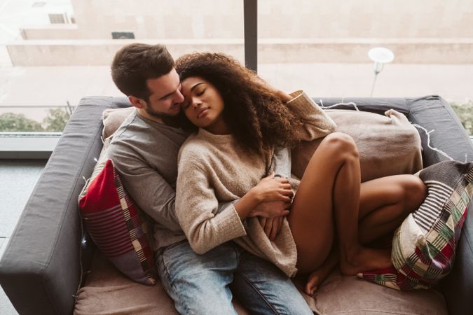 Young multiracial couple hugging on sofa