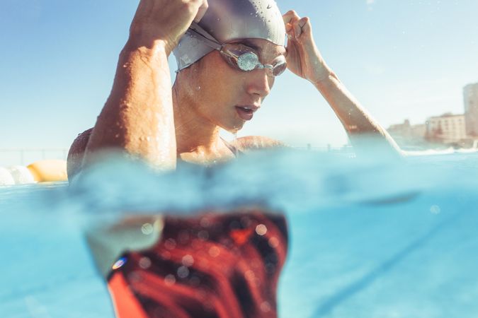 Close up of young woman swimmer inside the pool adjusting her goggles