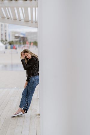 Smiling trendy woman leaning on white pillar on seashore