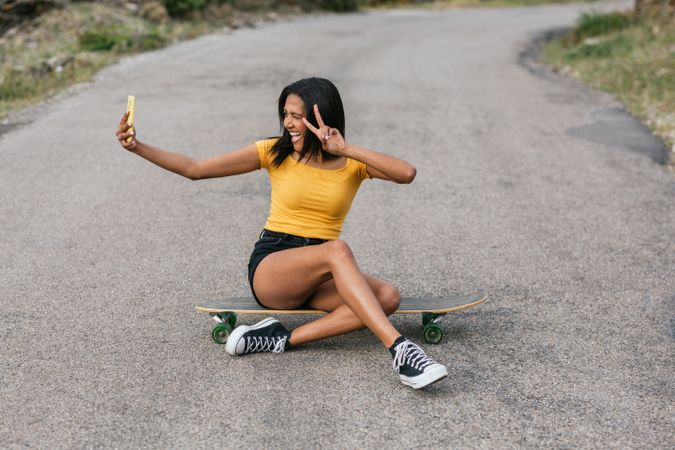 Delightful Latina woman on longboard taking selfie on smartphone
