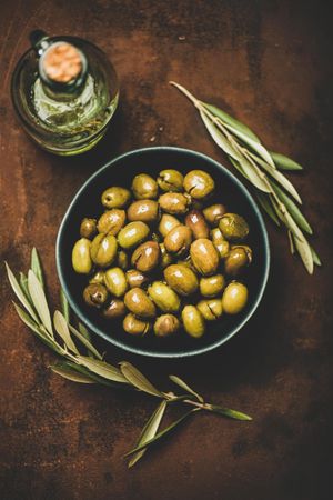 Bowl of olives on wooden table with garnish and bottle of olive oil