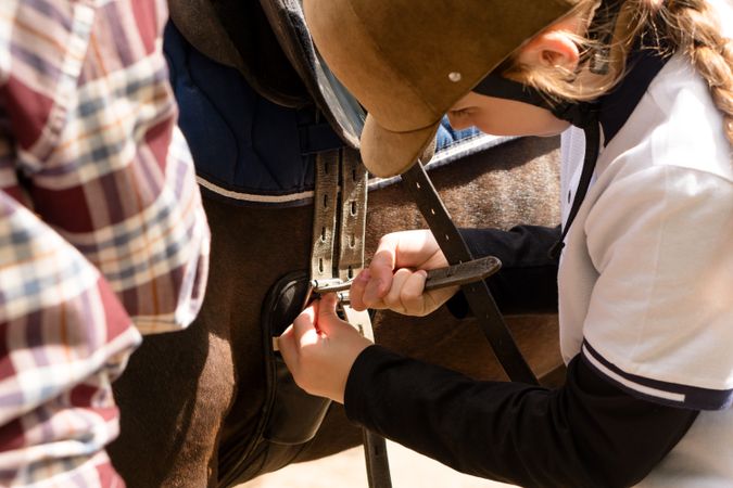 Young rider focused on adjusting horse saddle.