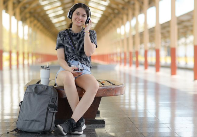 A young woman sits and listens to music while waiting for a train to travel