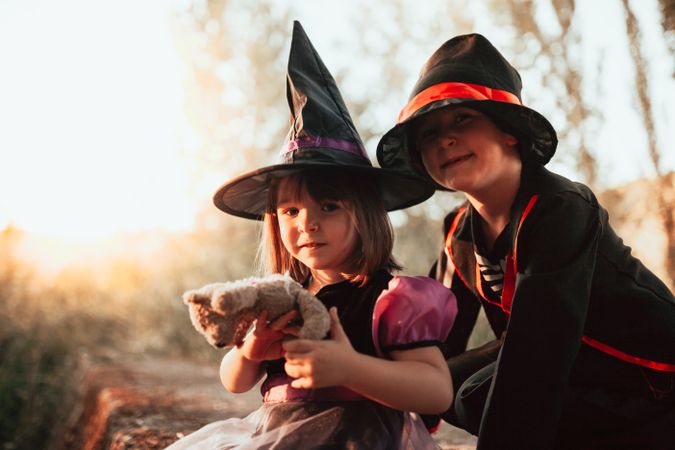 Brother and sister in halloween costumes sitting in the forest at dusk