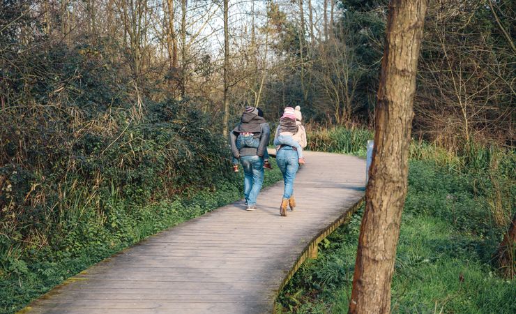 Back of mother and father giving their children piggy backs on forest trail