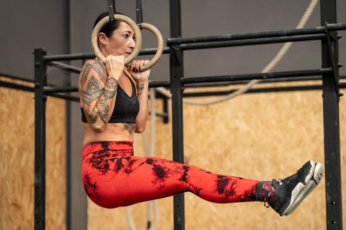 Strong female athlete doing pull ups using gymnastic rings in the gym