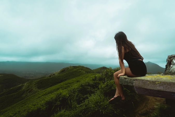 Woman sitting on cliff looking down mountains