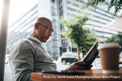 Man in eyeglasses sitting in a street side restaurant reading book 0VmLDb
