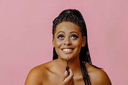 Happy Black woman applying lip gloss and looking up