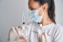 Woman in medical mask showing syringe with vaccine
