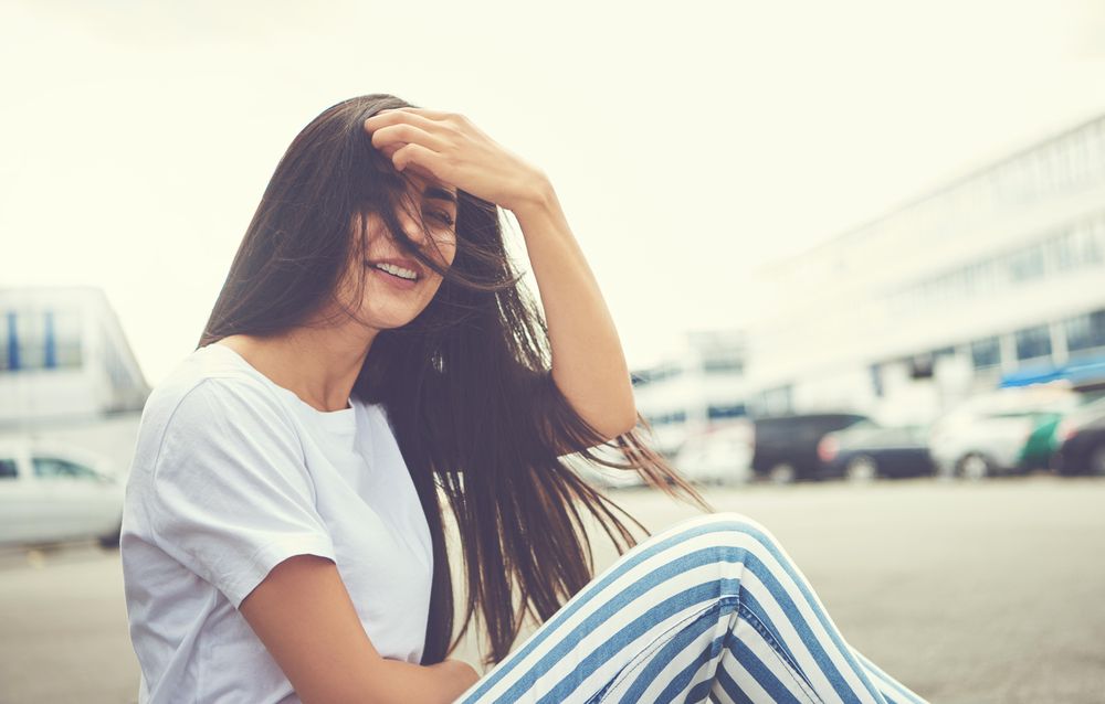 Woman sitting on curb brushing hair off her face