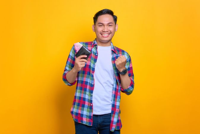 Thrilled Asian man smiling while holding wallet and making fist