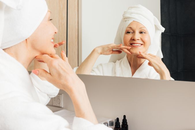 Smiling woman with hair wrapped in towel looking in hotel bathroom mirror