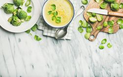 Brussels sprout soup, garnished with fresh sprouts, next to wooden board, copy space
