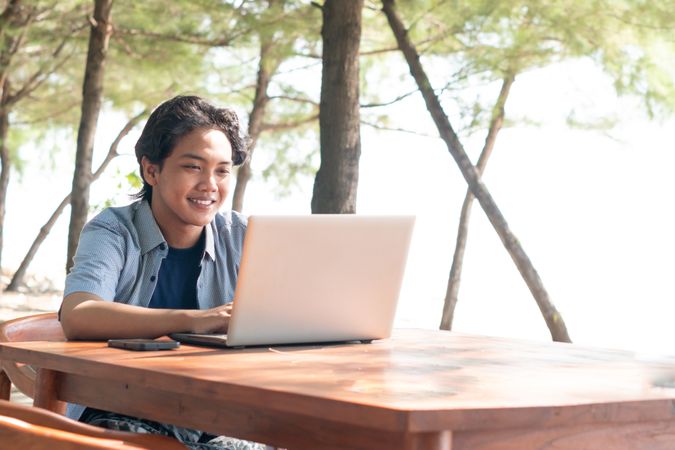 Happy Asian Young businessman work at outdoor with laptop. Concept of remote and freelance work. Young successful man wearing casual blue cloth.