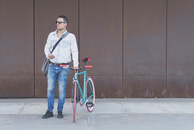 Male in sunglasses standing with red and green bicycle and looking around