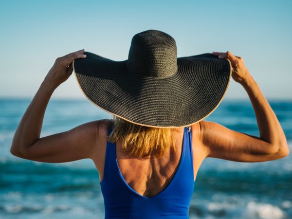 Woman in blue swimsuit and hat on sandy beach