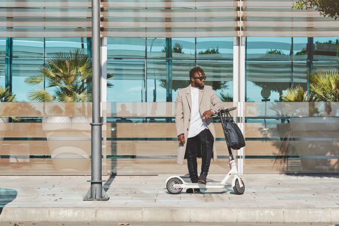 Stylish Black man with scooter standing on side path