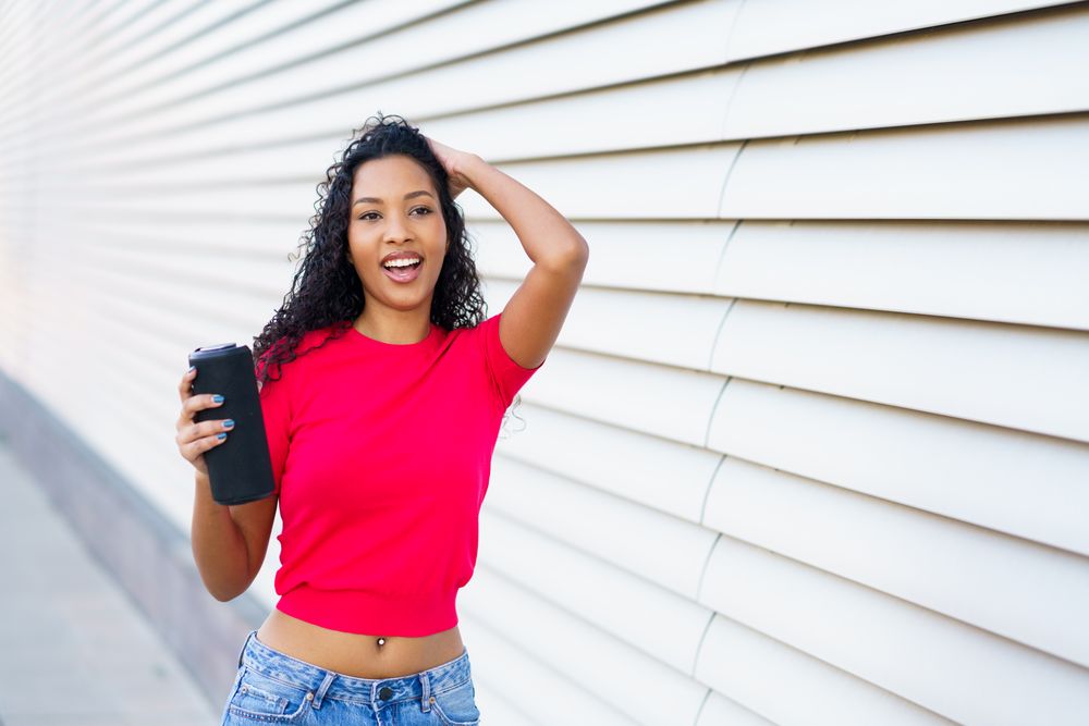 A Joyful Young Woman Posing Happily with Her Phone Against a Vibrant Modern Background