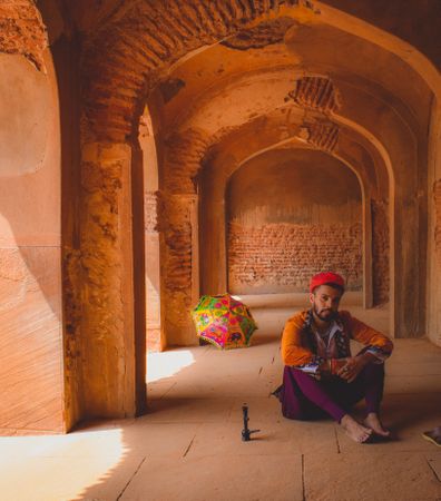 Man in traditional outfit sitting in hallway beside umbrella