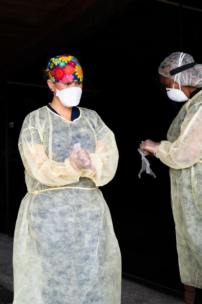 Two nurses stand near each other putting on PPE