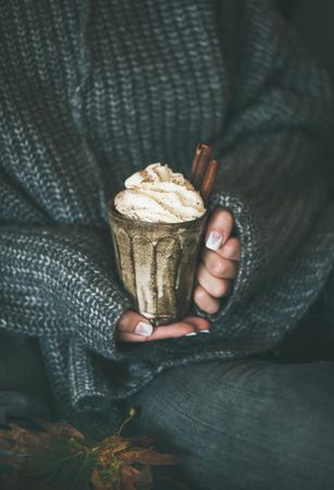 Woman in cozy sweater holding whipped cream topped drink