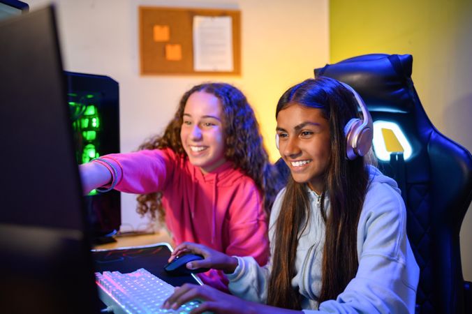 Cheerful teenage diverse sitting at table with gaming PC and playing game