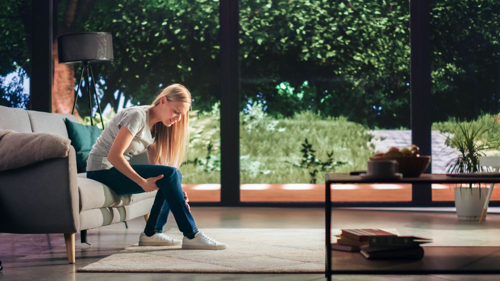 Young Adult Female Had to Sit Down on a Couch at Home Due to Discomfort in a Result of Leg Trauma or Arthritis.